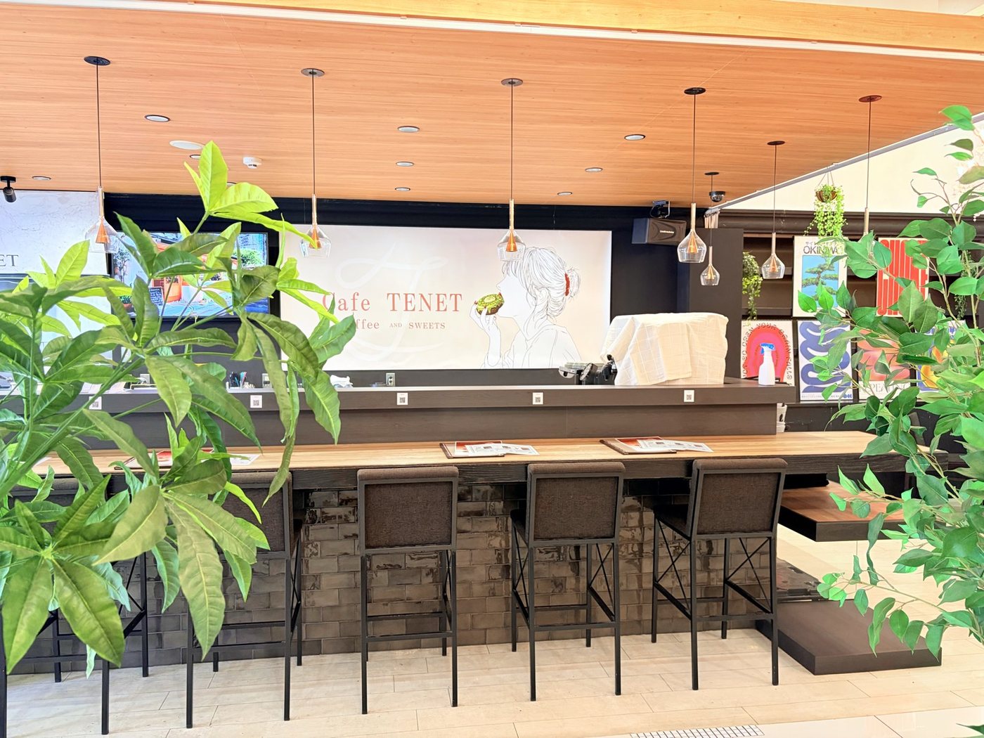 Cafe TENET 福井 — 観葉植物越しに見えるカウンター席とウェルカムアート